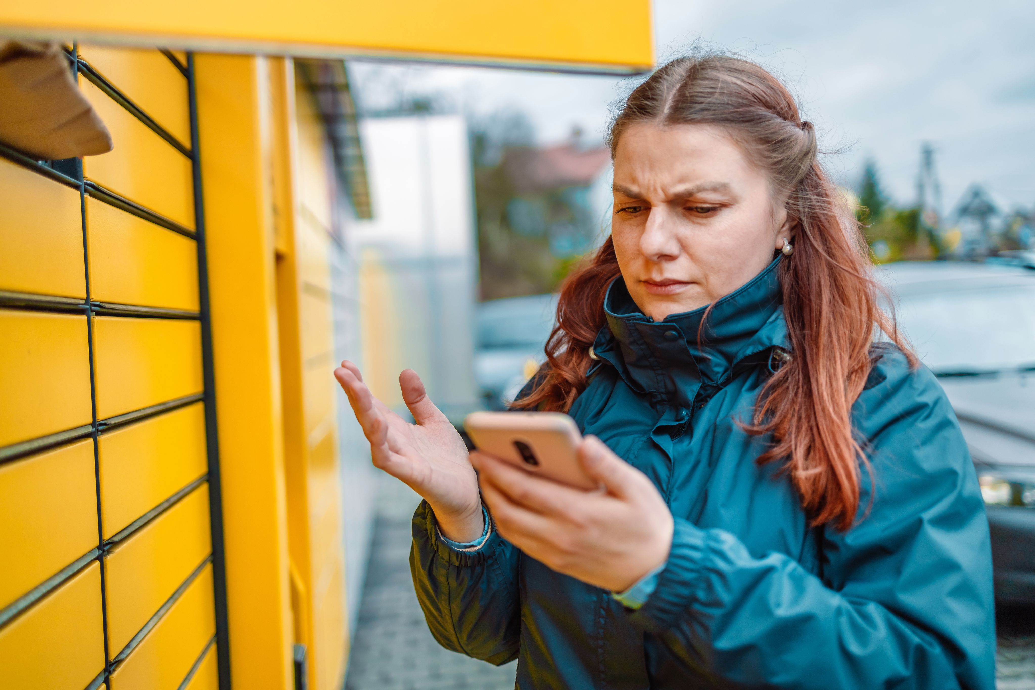 Frustrated woman looking at smartphone in front of yellow package lockers